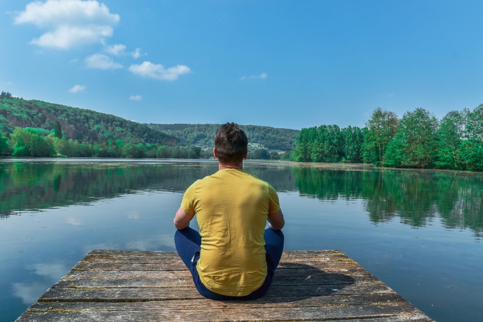 Person sitting peacefully by a lake, reflecting the benefits of aligned decision making.