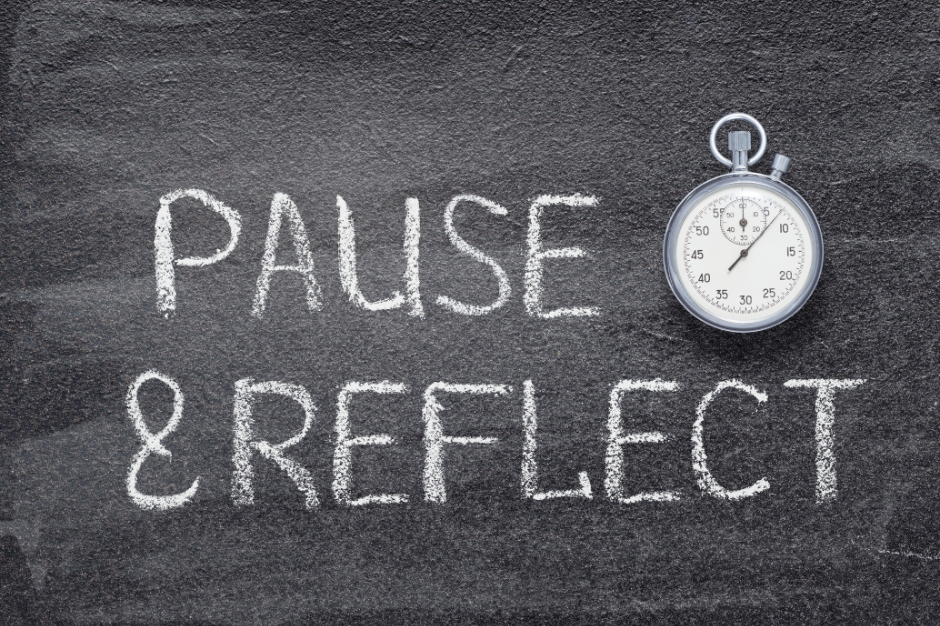 Stopwatch resting on a blackboard with the words 'PAUSE & REFLECT' written in chalk, symbolizing the importance of taking time for reflection.